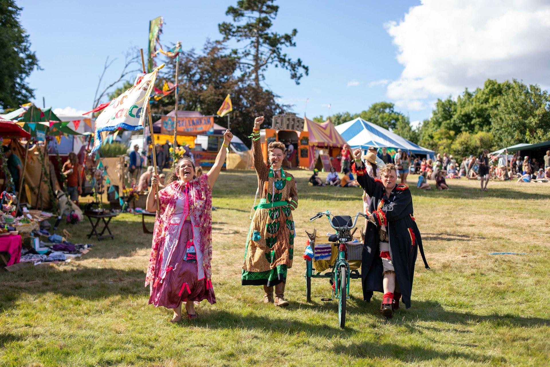 Festival goers surrounded by colorful tents and flags in a field enjoying the Green Gathering festival, Wales 